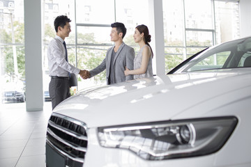 Young couple buying car in showroom
