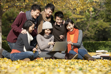 Cheerful college students with laptop and books on campus in a beautiful autumn day