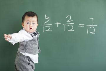 Cute baby doing mathematics on blackboard