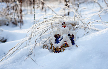 Игрушечный домик в снежном сугробе, освещённом солнцем.
