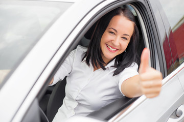 Fototapeta premium Woman showing thumbs up while driving her new car 