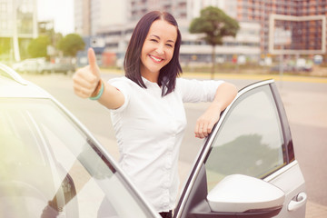 Happy woman standing next to her car  and showing thumbs up 
