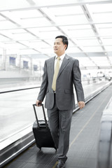 Mature businessman with wheeled luggage on airport escalator