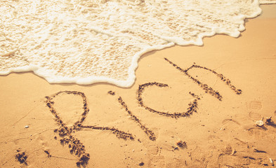rich word written on sand , investment concept