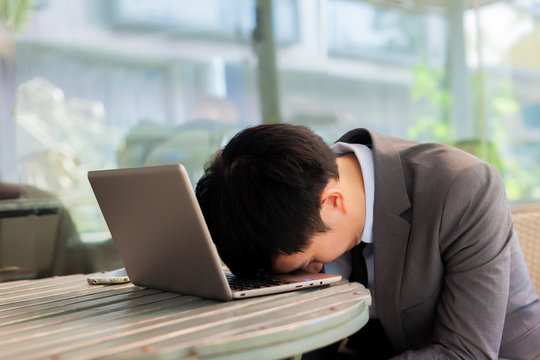 Businessman tiring and sleeping on his laptop in outdoor scene