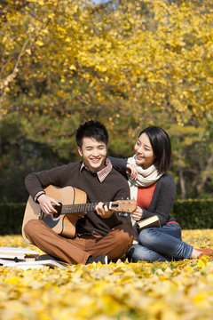 Happy college couple with guitar and books enjoying the sunny autumn on campus