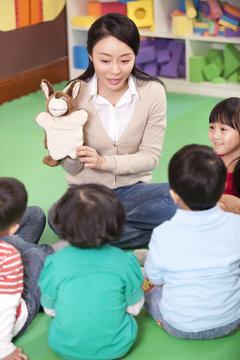 Female teacher playing hand puppet game with cute kindergarten children