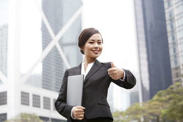 Happy businesswoman doing thumbs up with portfolio in hand, Hong Kong