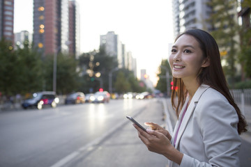 Young woman waiting for taxi with smart phone