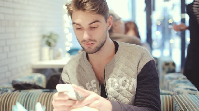 Young man with smartphone sitting in cafe, close-up