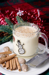Christmas Eggnog – A cup of eggnog with grated nutmeg and cinnamon on top. Christmas decorations in the background.