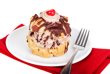 Cream Puff on White Plate – A chocolate cream puff with chocolate on top and a cherry on a white plate. On a white background.