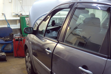 Gray color passenger car with open hood undergoing repairs indoor in the service station