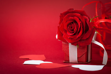 Prettily developed rose lying on gift box surrounded by hearts. Red matte background. White and red...