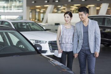 Young couple looking at new car in showroom