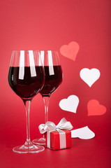 Fototapeta na wymiar Valentine’s day - wine glasses, hearts and elegant gift box. Vertical position. Red matte background. White and red elements.