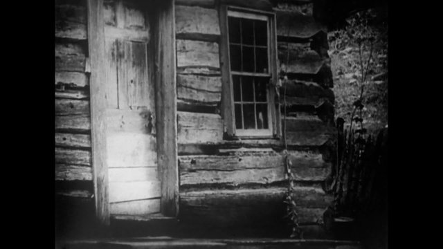 Exterior of log cabin with door opening and shutting, 1920s