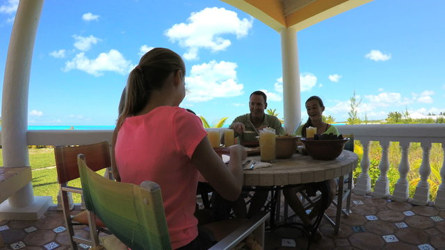 Caucasian parents daughters eating lunch on deck of tropical beach resort 