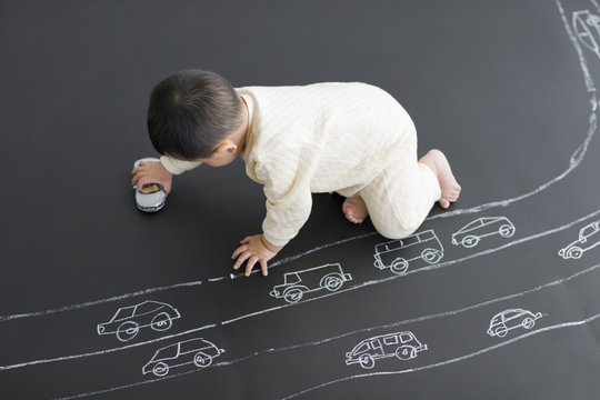 Cute baby playing with toy car on drawing board