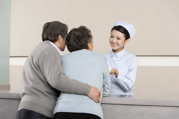 Young Nurse Helping Senior Couple at Nurses' Station