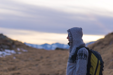 Hooded lady with backpack resting on the Alps at sunset