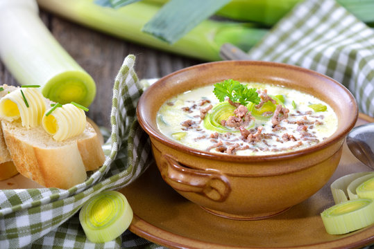 Deftige Hackfleisch-Lauch-Suppe in der handget&ouml;pferten Suppenschale mit Butter-Baguette auf Holztisch serviert