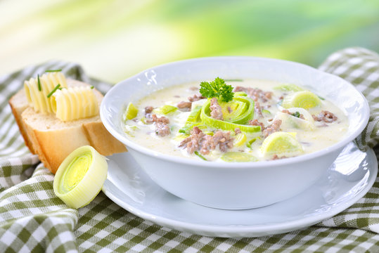 Deftige Lauch-K&auml;se-Suppe mit Hackfleisch und Butter-Baguette vor softigem Lauchhintergrund serviert