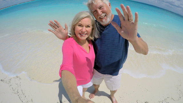 Smiling Caucasian senior couple on beach in casual clothing taking a selfie
