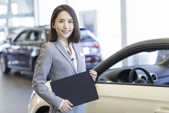 Confident saleswoman standing with new cars in showroom
