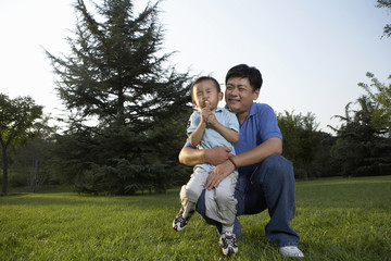 Father Holding Son As He Blows A Dandelion