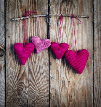 Crochet pink hearts on wooden background. Toned image