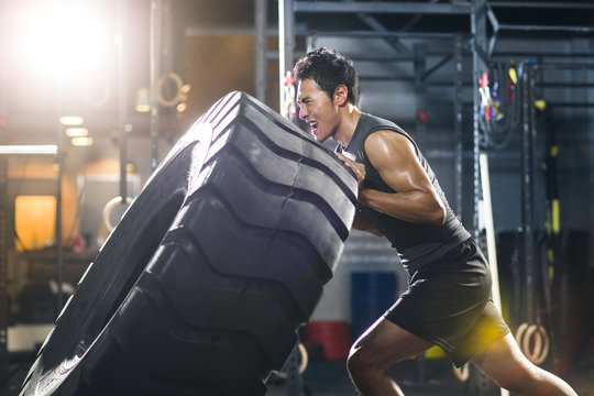 Young man pushing large tire in crossfit gym