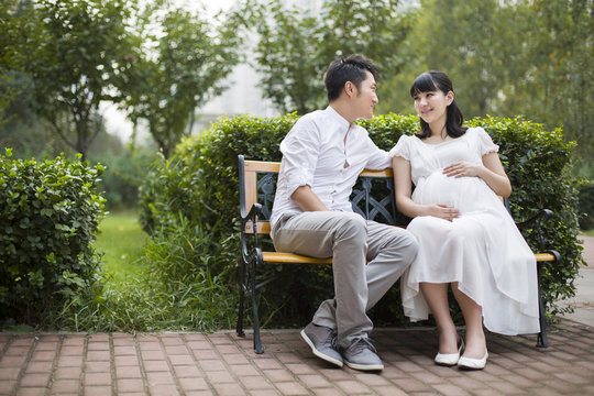 Pregnant woman and her husband sitting on bench