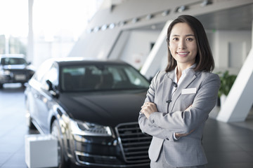 Confident saleswoman standing with new cars in showroom