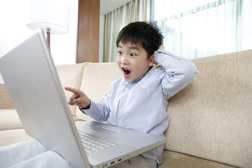 Young boy points at laptop screen on sofa