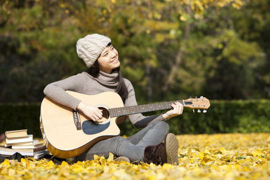 Lovely female college student with guitar and books enjoying the fine weather of autumn