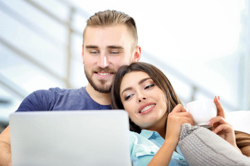 Fototapeta premium Happy couple sitting on sofa with coffee and working on a laptop