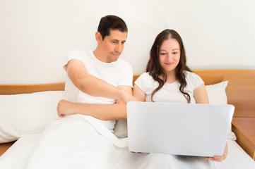 happy couple using laptop on the bed