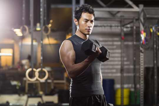 Young man lifting weights at gym - Powered by Adobe