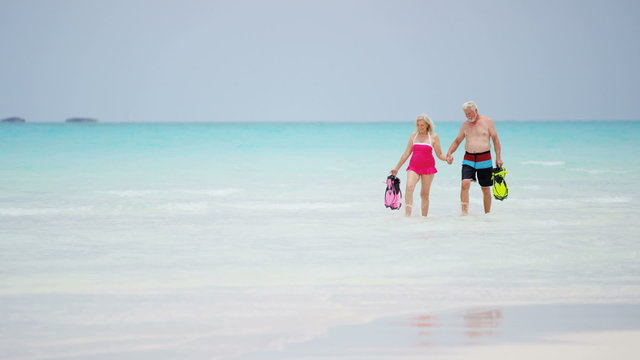 Retired couple in swimwear on a tropical beach with snorkel equipment