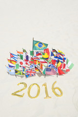 Golden 2016 sign sitting on smooth sand beach with international flags flying nearby in Rio de Janeiro Brazil