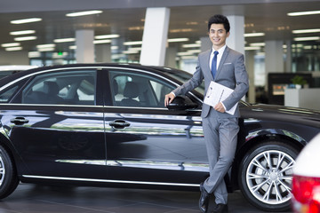 Confident salesman standing with new car in showroom