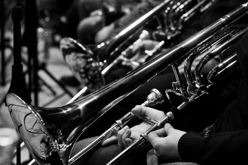 Trombones in the hands of the musicians in the orchestra in black and white