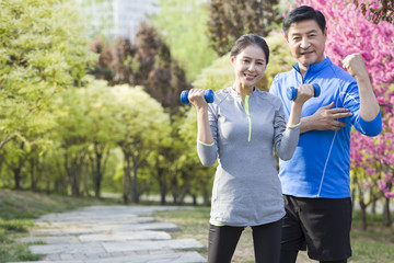 Happy mature couple exercising with dumbbell in park