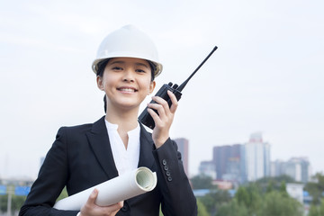 Young female architect with intercom and blueprint outdoors