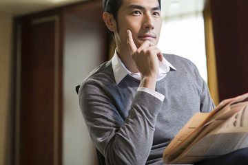 Young businessman reading newspaper in study