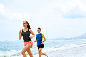 Exercising. Happy Smiling Sporty Runner Couple Running On Beach. Athletic Woman And Fit Man Jogging Near Sea ( Ocean ) During Outdoor Workout. Sports, Fitness. Healthy Lifestyle. Health Concept