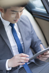 Businessman using digital tablet in car back seat