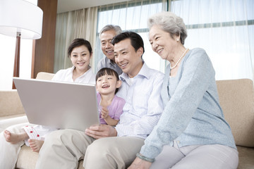 Fototapeta premium Grandparents and Parents with daughter look at Laptop on a sofa