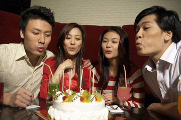 Group of Young People Blowing Out Candles On Birthday Cake